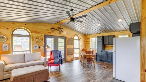 A spacious interior with a wooden floor, a dining area, a kitchen, and a living room with a sofa and ottoman. - Melbourne Home w/ Fire Pit on the White River! (Melbourne)