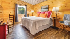 A wooden cabin bedroom with a bed, two bedside tables, a chair, a window with curtains, and a ceiling fan. - Melbourne Home w/ Fire Pit on the White River! (Melbourne)