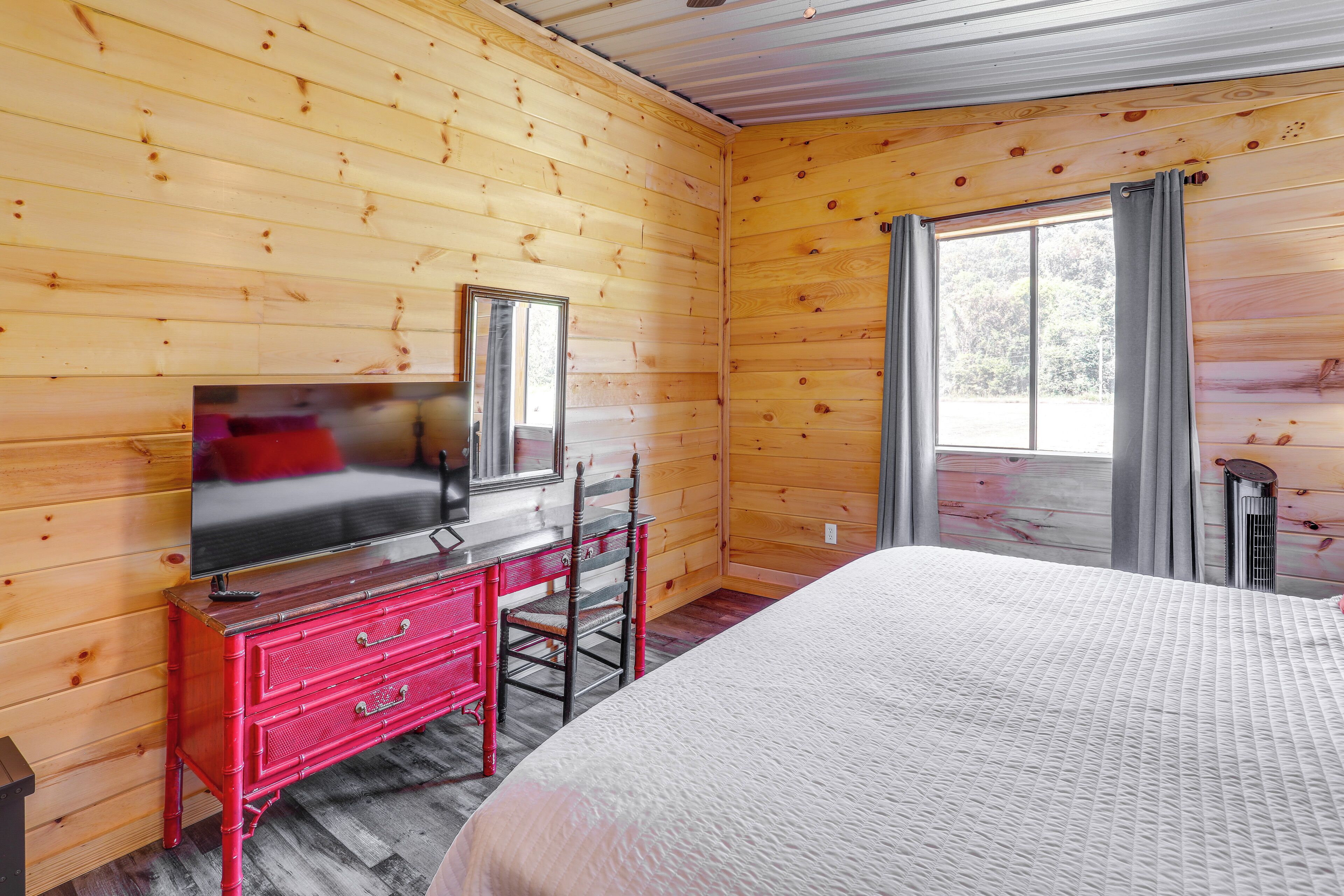 A wooden-paneled room with a bed, a red dresser, a television, and a window with curtains.