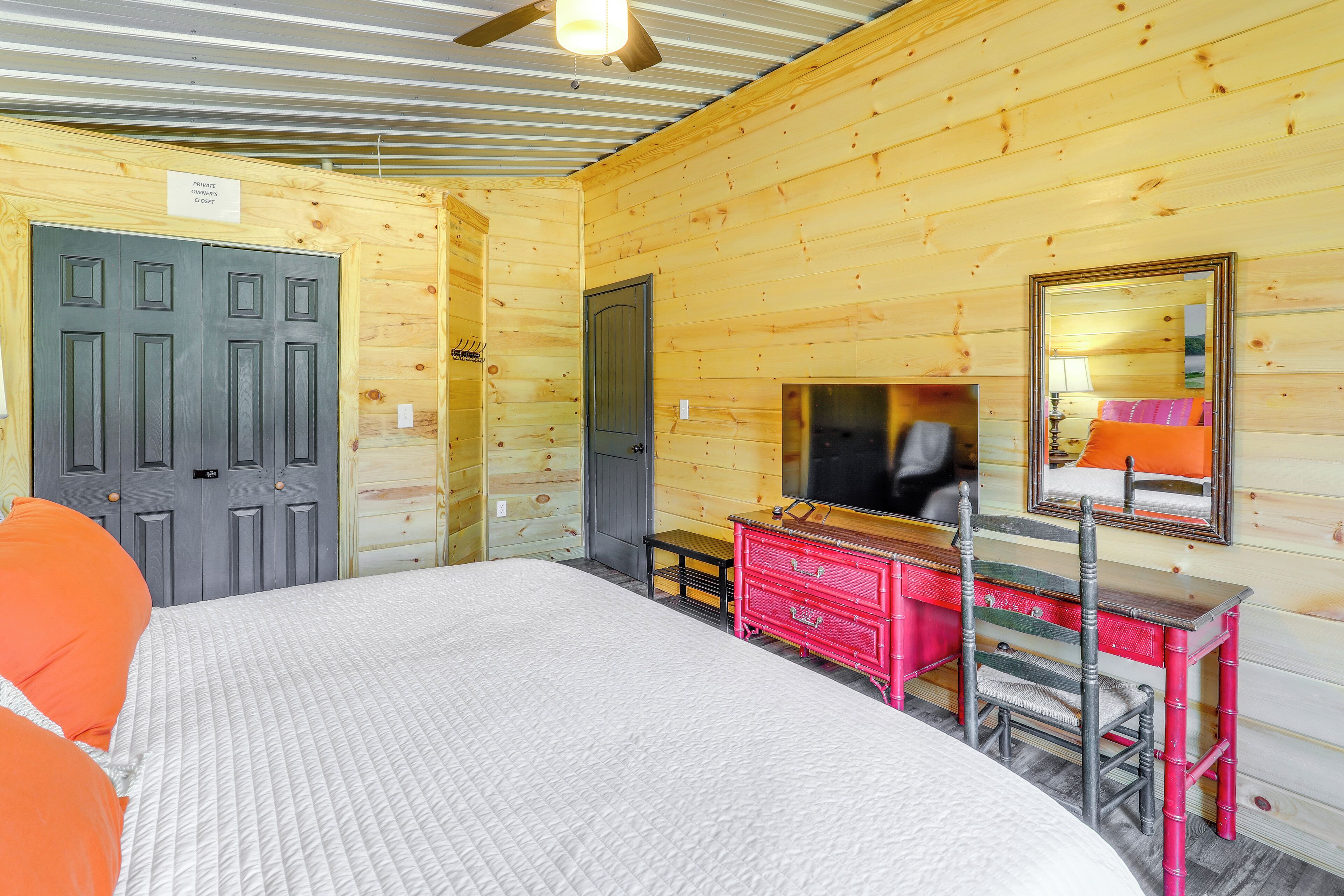 A wooden cabin room with a bed, dresser, mirror, and a door.