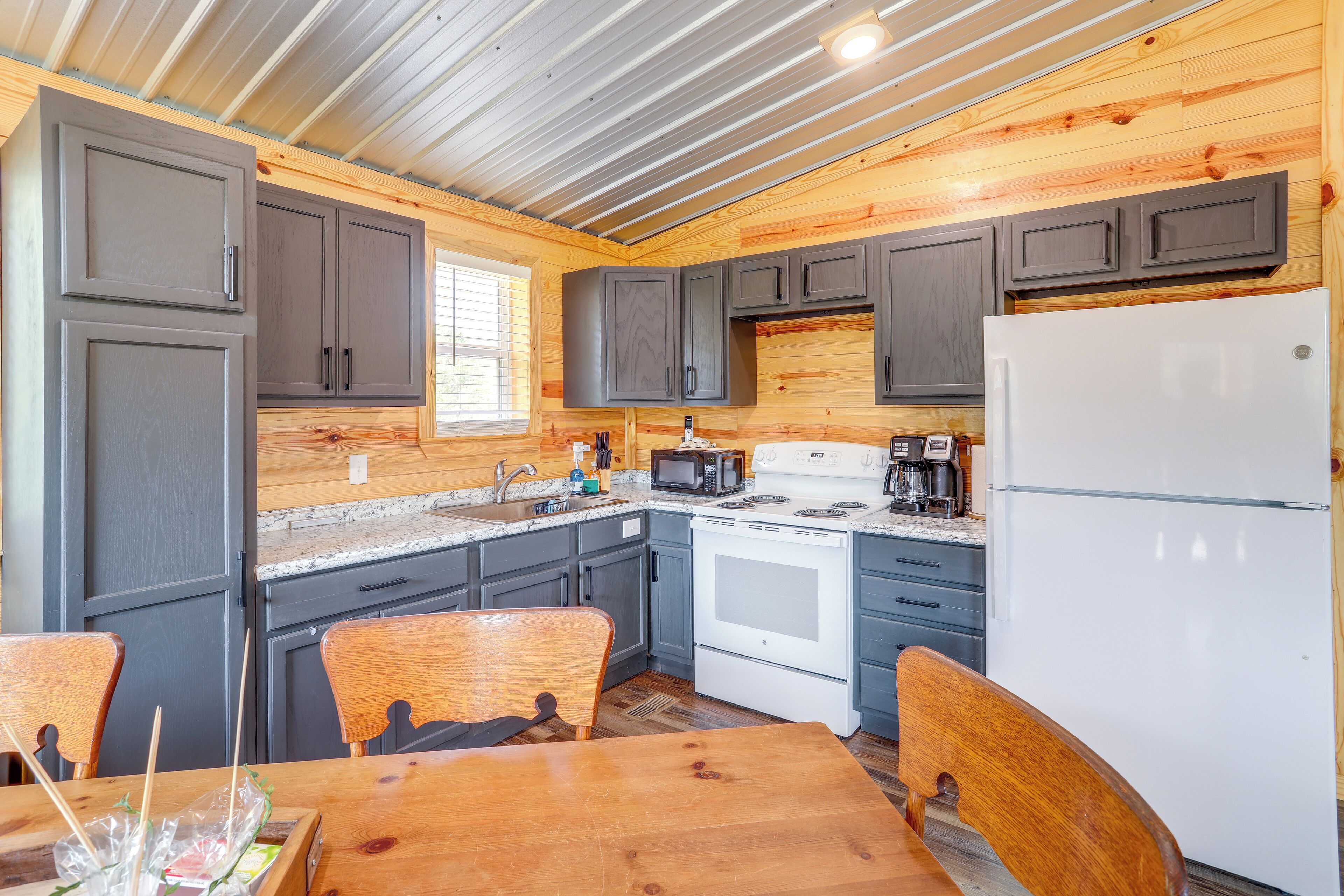 A compact kitchen with grey cabinets, a white refrigerator, a microwave, and a stove.
