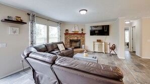 A living room with a fireplace, leather sofa, and a flat-screen TV. - Efficiently Equipped Lewis Home: Deck & Gas Grill! (Lewis)