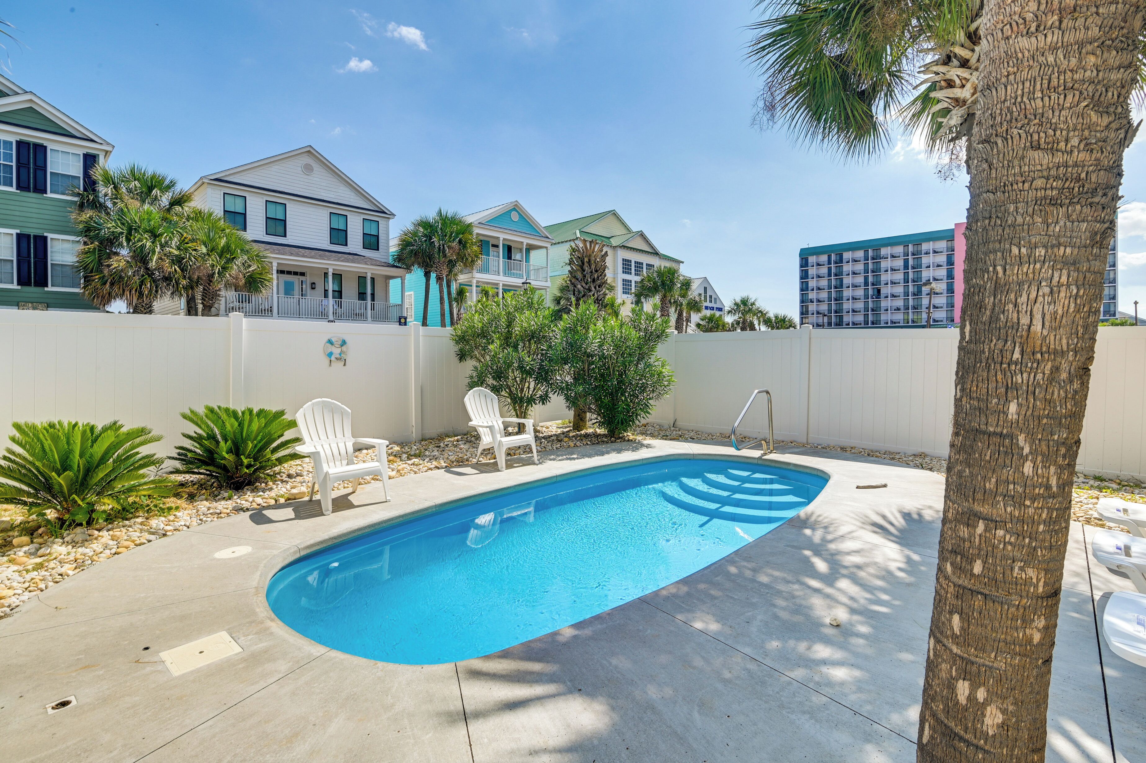A swimming pool with a white fence, two white chairs, and a palm tree.