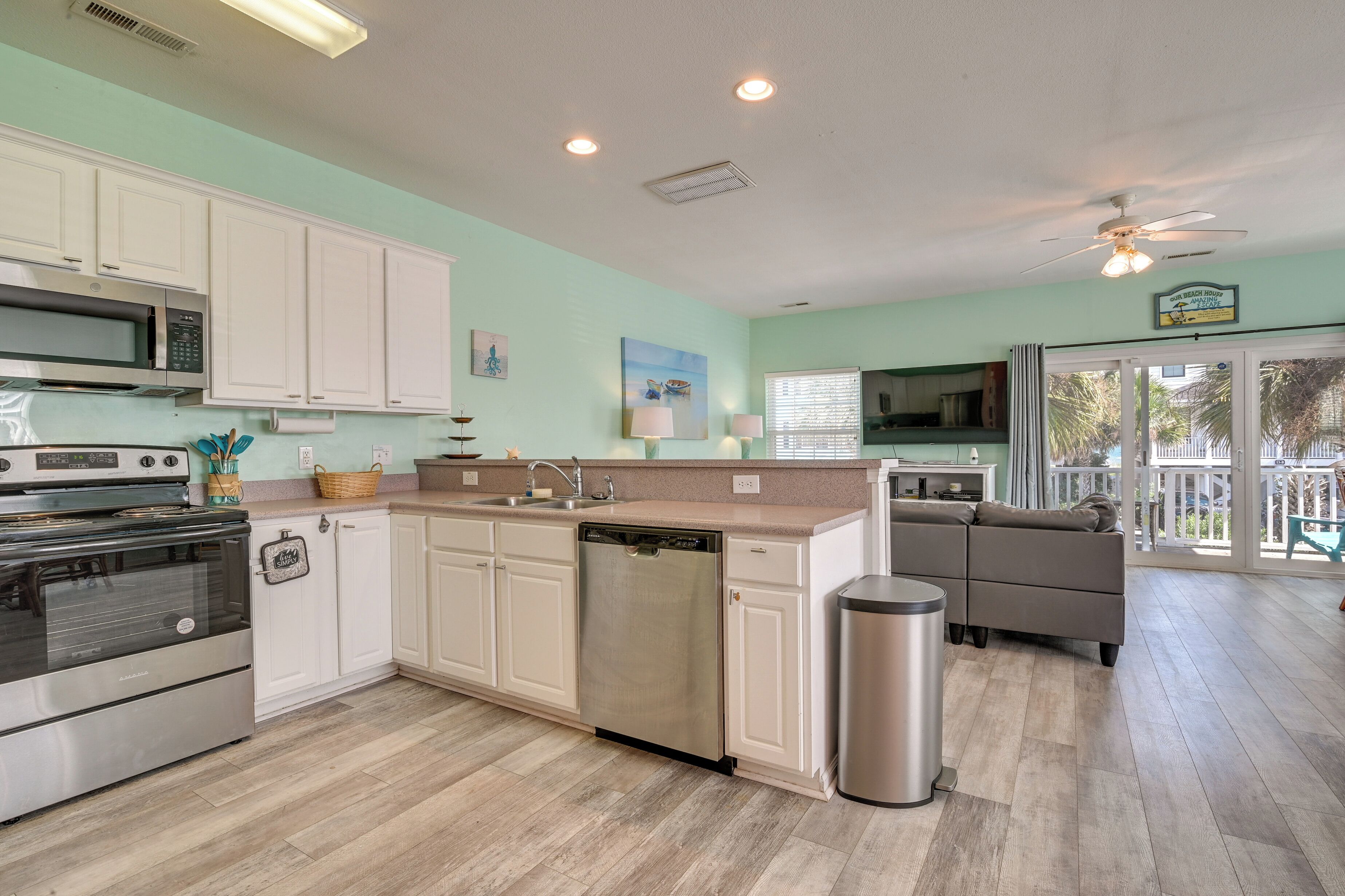A modern kitchen with white cabinets, stainless steel appliances, and a wooden floor.