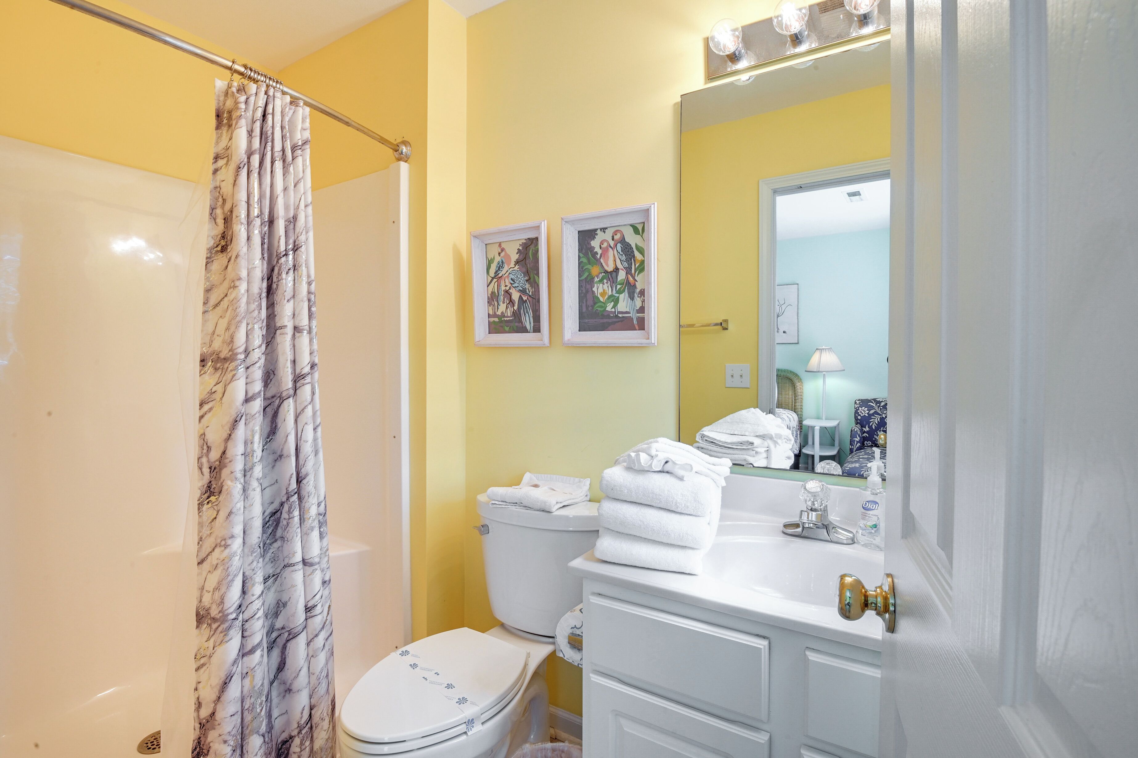 A bathroom with a yellow wall, a white toilet, a sink with a mirror, and a shower curtain.