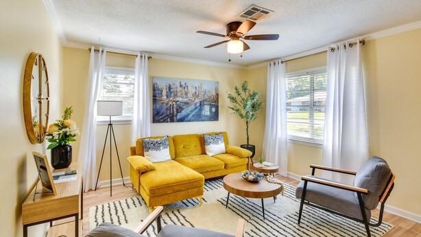 A living room with a yellow sofa, a grey armchair, a round coffee table, a floor lamp, and a painting of a cityscape. - Lovely Montgomery Home ~ 7 Mi to Downtown! (Montgomery)