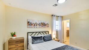 A bedroom with a bed, a dresser, a nightstand, a painting, and a door leading to another room. - Lovely Montgomery Home ~ 7 Mi to Downtown! (Montgomery)