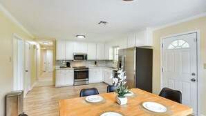 A modern kitchen with white cabinets, stainless steel appliances, and a dining area with a wooden table set for four. - Lovely Montgomery Home ~ 7 Mi to Downtown! (Montgomery)