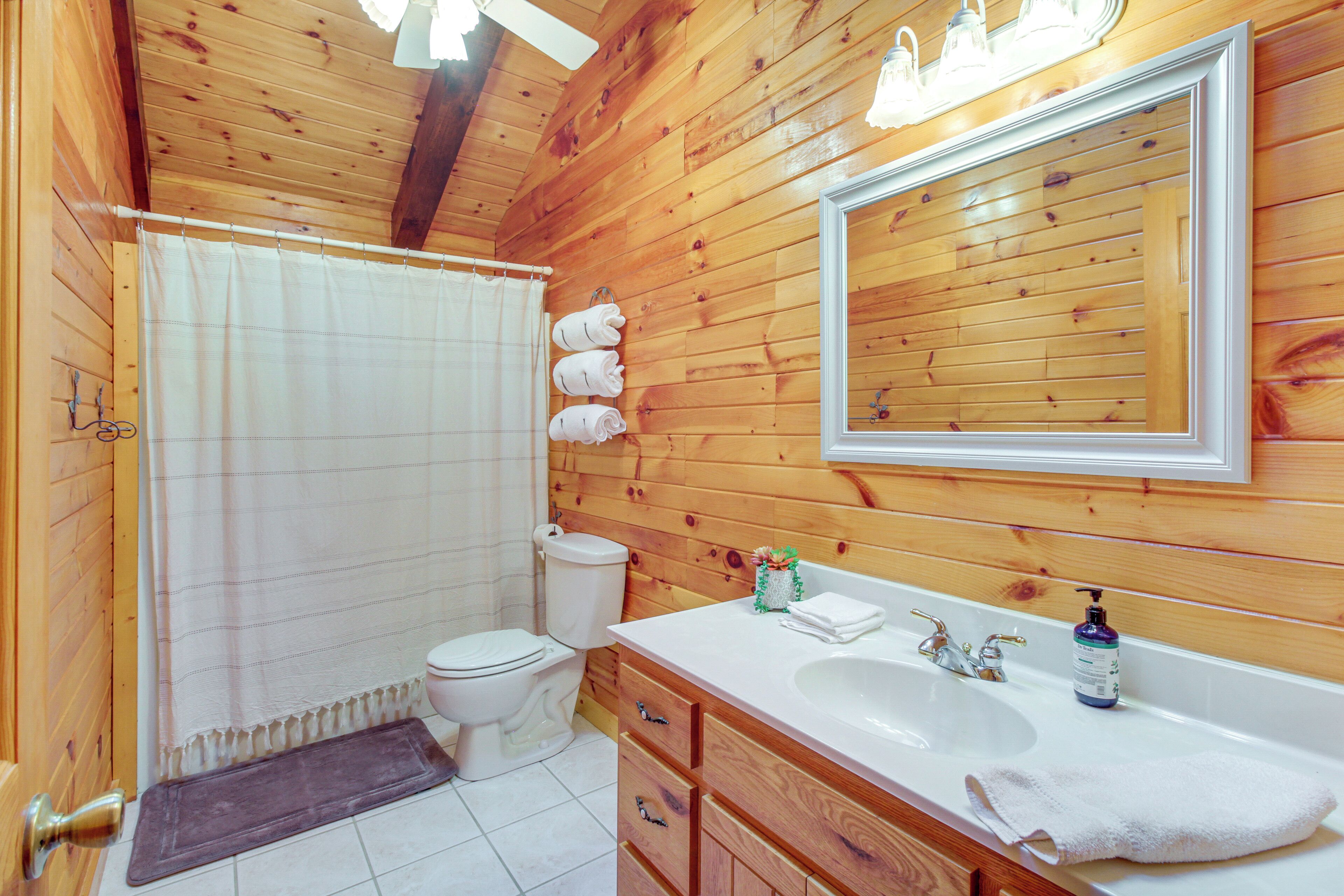 Ein Badezimmer mit Holzwandverkleidung, einem weißen Waschbecken, einem Spiegel und einer Toilette.