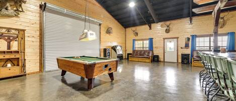 A spacious indoor area with a pool table, wooden walls, and mounted animal heads.