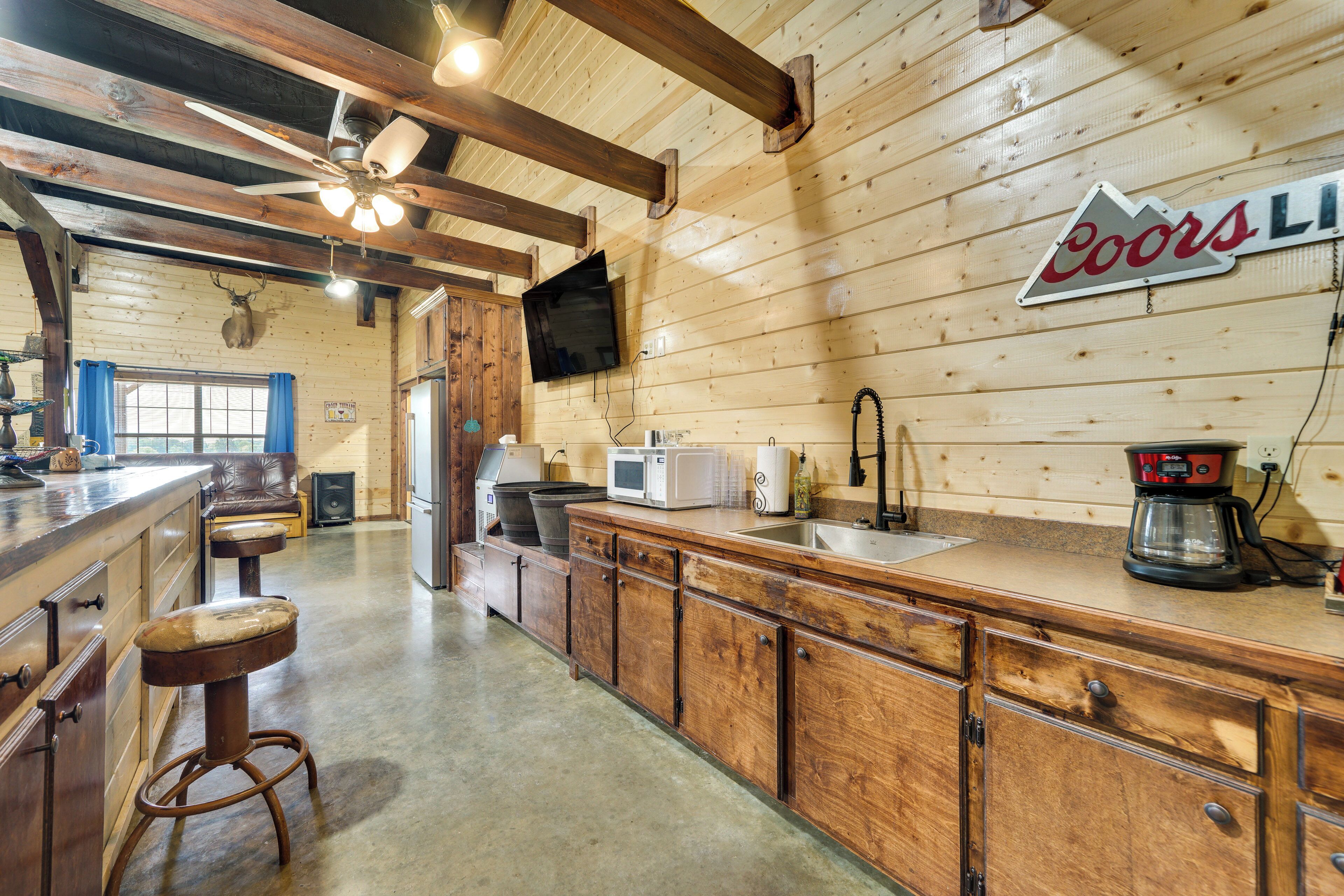 L’intérieur d’un chalet en bois comprend un coin cuisine, des tabourets de bar, un téléviseur et une enseigne Coors Light.