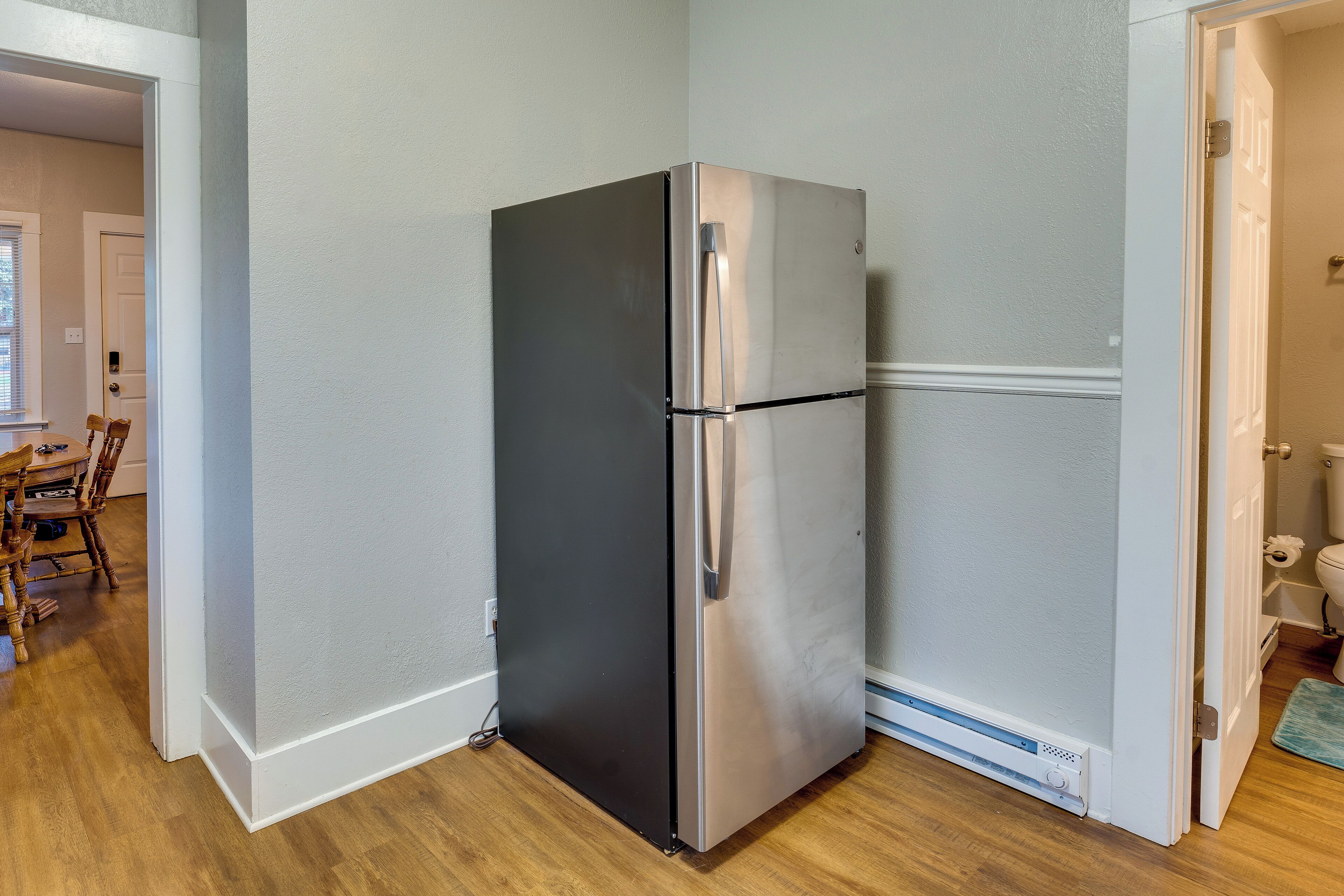 A compact kitchen with a stainless steel refrigerator, wooden dining table, and chairs.