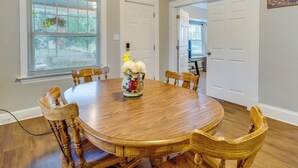 A dining room with a wooden table and chairs, a vase with flowers, and a window with blinds. - Spokane Vacation Rental w/ Central Location! (Spokane)