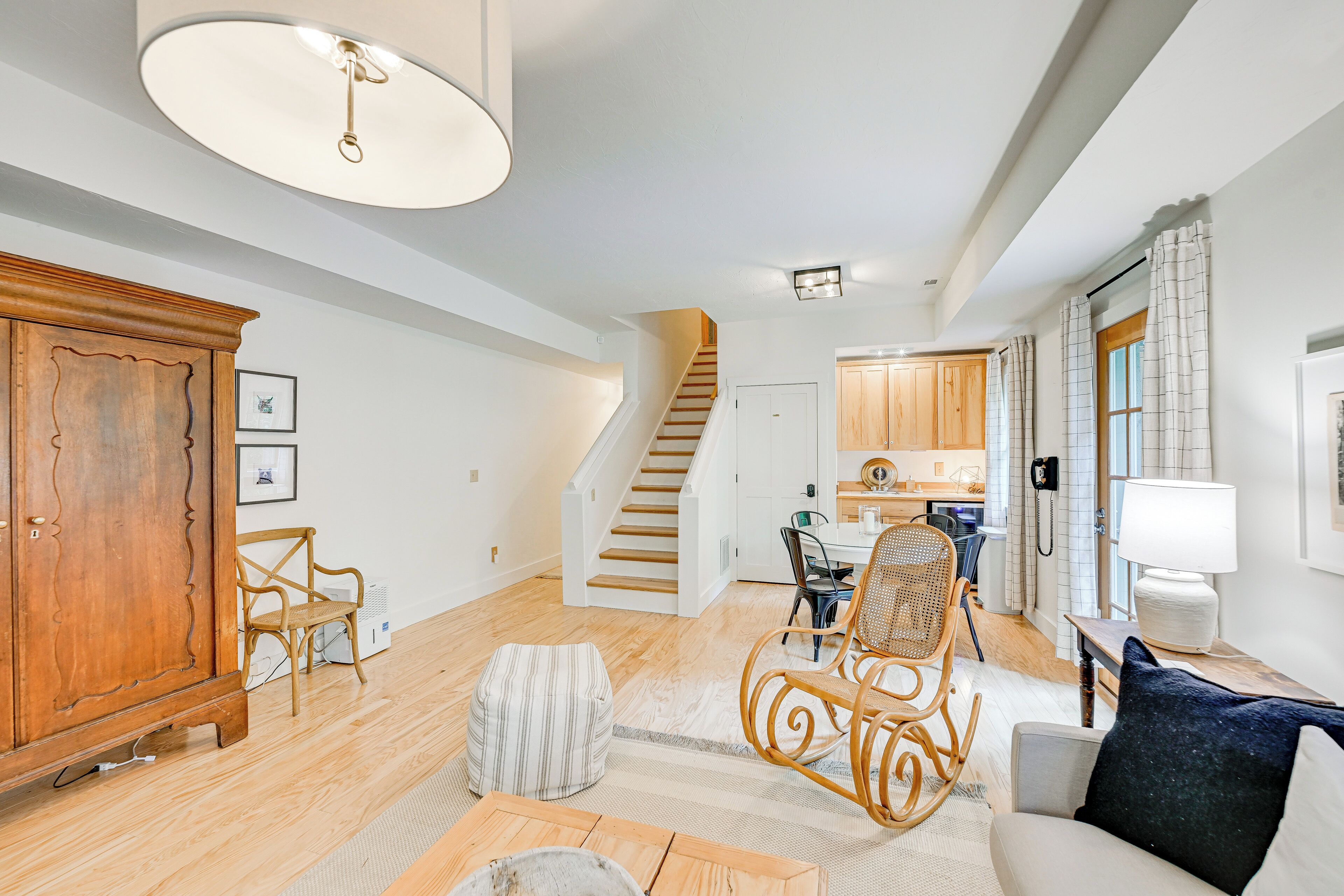 A spacious living area with a staircase, wooden furniture, and a kitchen in the background.