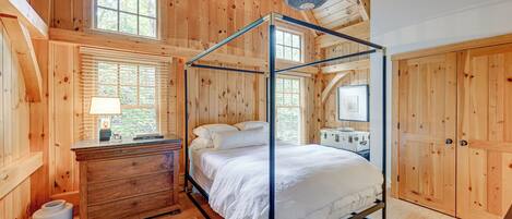 A wooden cabin bedroom with a four-poster bed, a dresser, and a window with blinds.