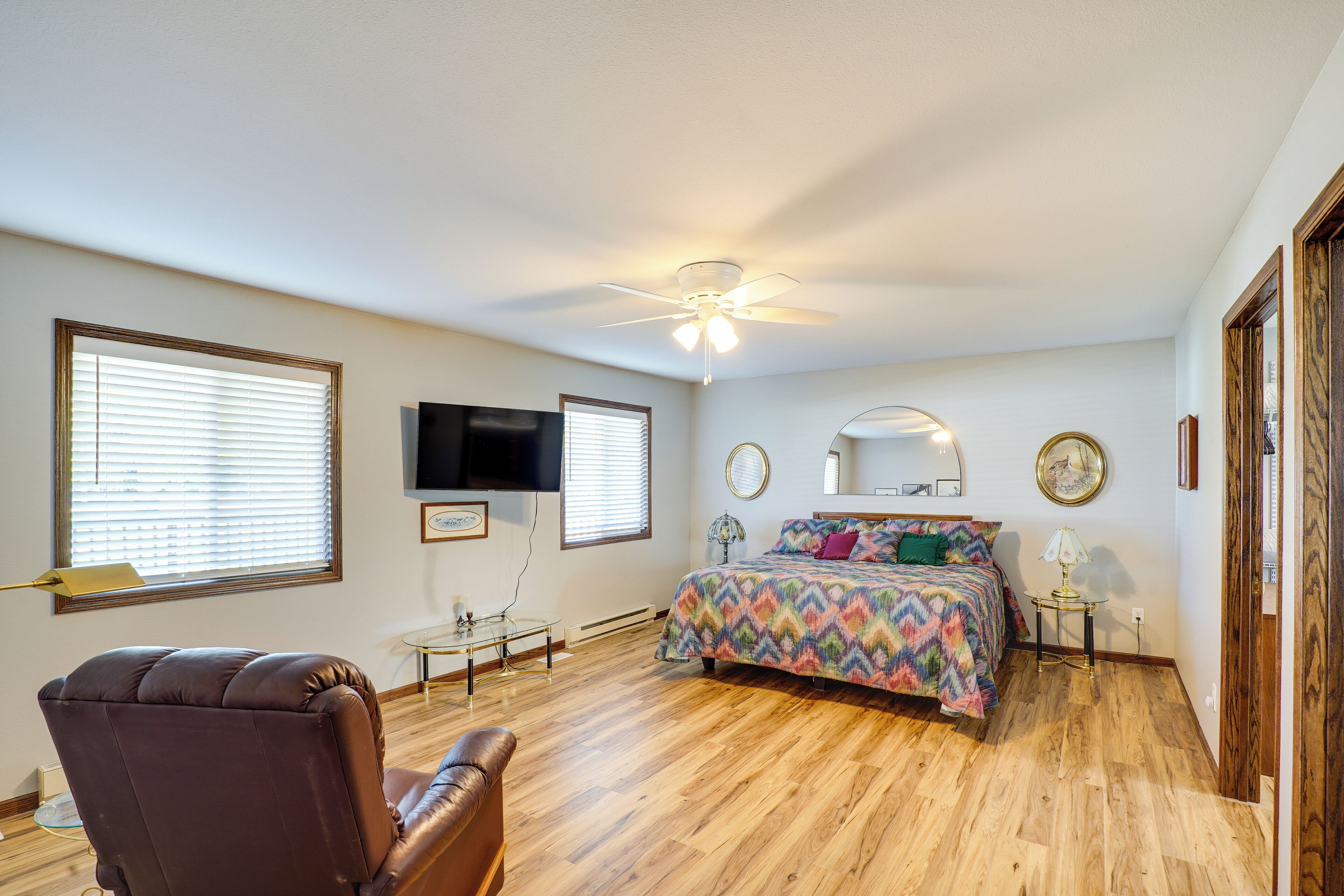 A bedroom with a bed, a chair, a ceiling fan, and a TV.