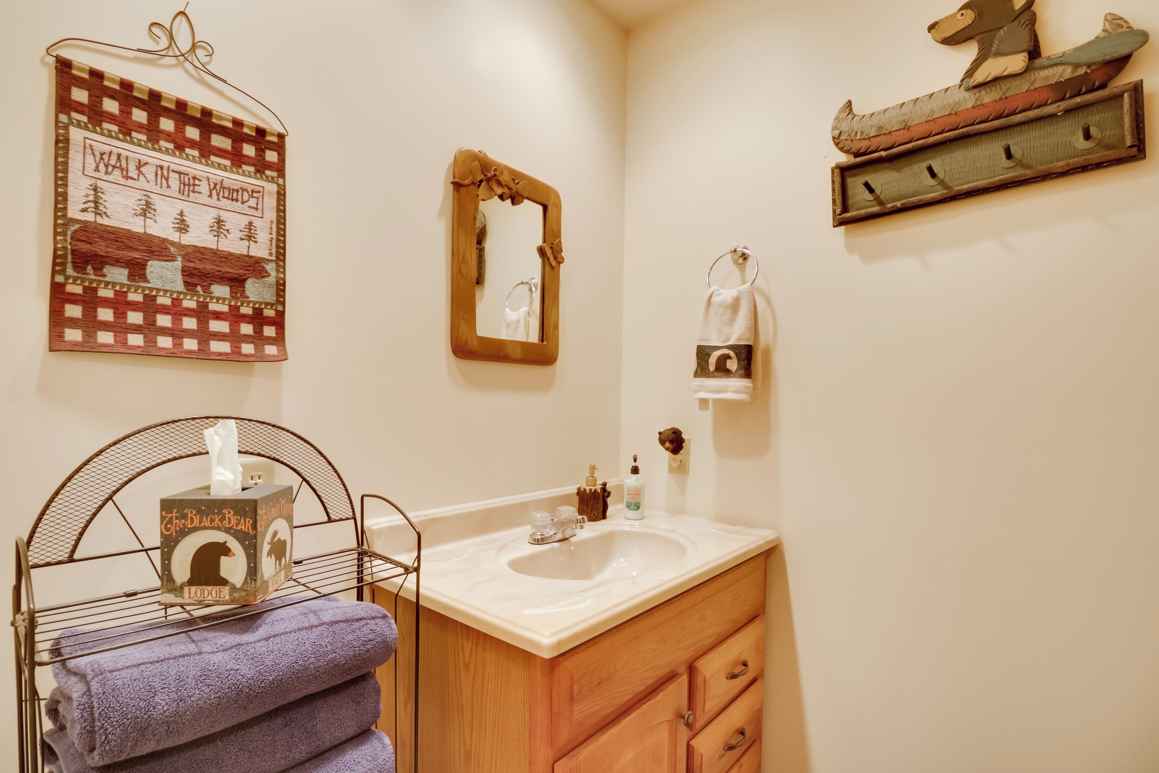Un baño con lavamanos, espejo, toallero y un letrero decorativo.