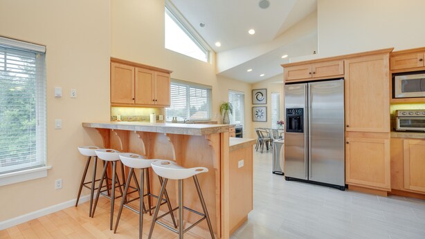 Una cocina moderna con gabinetes de madera, un refrigerador de acero inoxidable y una barra con taburetes.