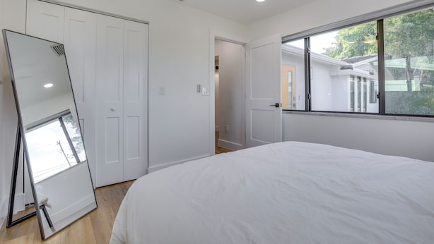 A bedroom with a large bed, a sliding door closet, and a window with a view of the outside. - Chic Florida Retreat w/ Pool, Patio & Gas Grill! (Wilton Manors)