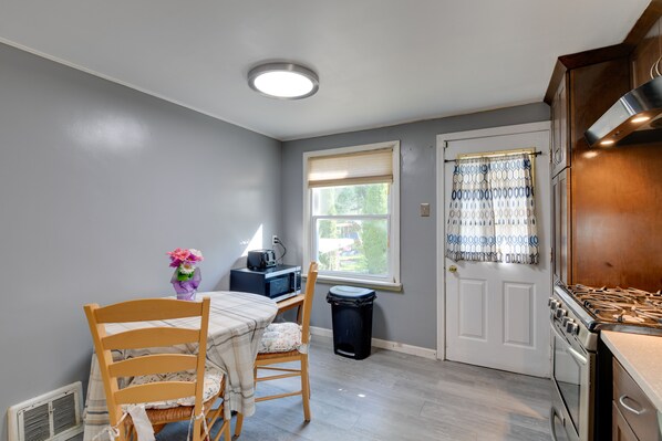 A kitchen with a dining table, chairs, a microwave, a stove, and a trash can.