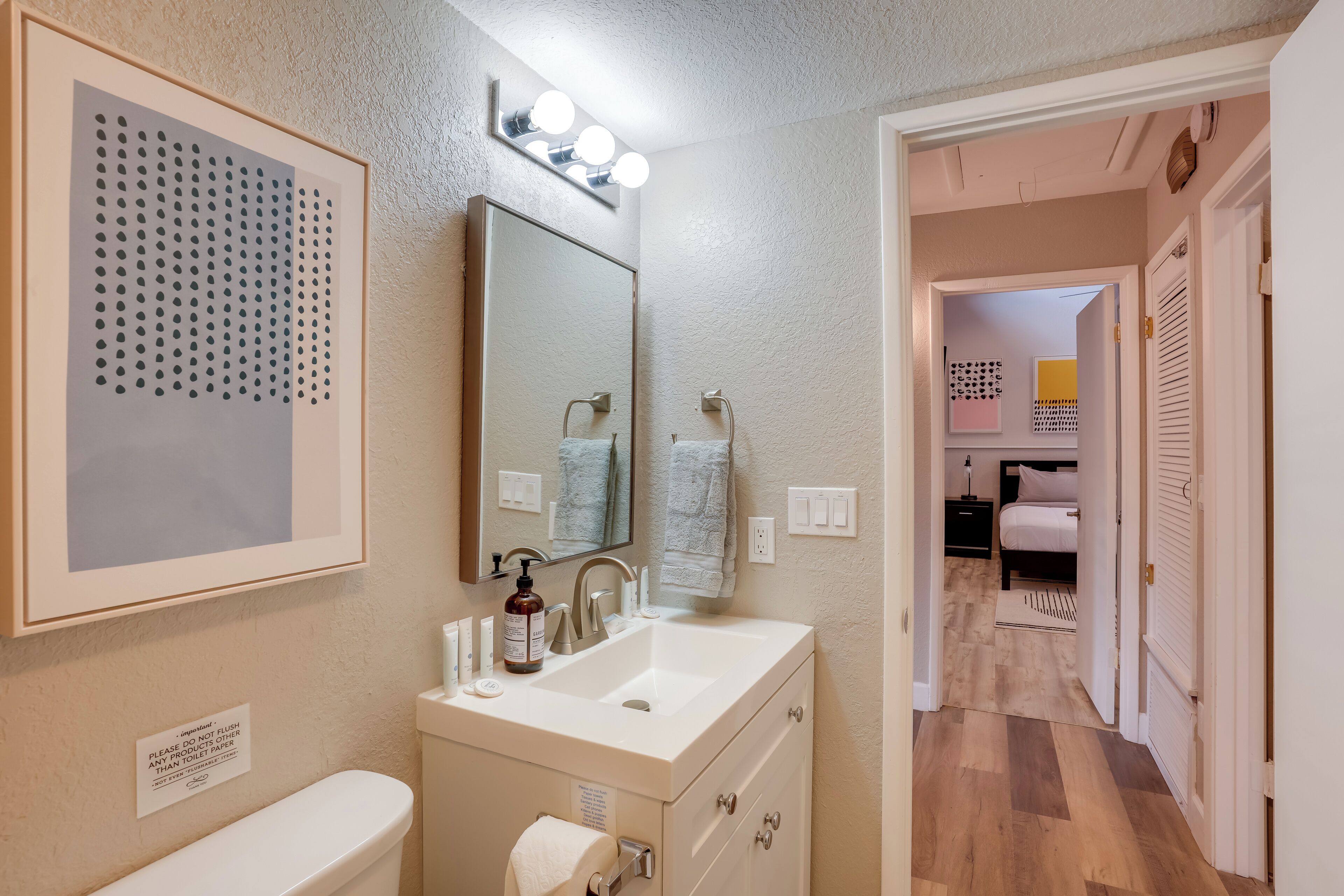 A bathroom with a sink, mirror, and a framed dot-patterned artwork.