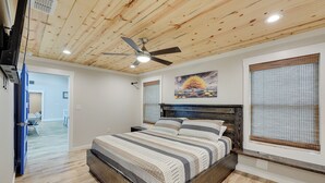A bedroom with a wooden ceiling, a bed with striped bedding, a ceiling fan, and a painting on the wall. - Riverfront 'caddo Shack' Home w/ Views & Fire Pit (Glenwood)