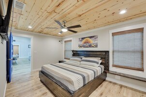Um quarto com teto de madeira, uma cama com roupa de cama listrada, um ventilador de teto e um quadro na parede.