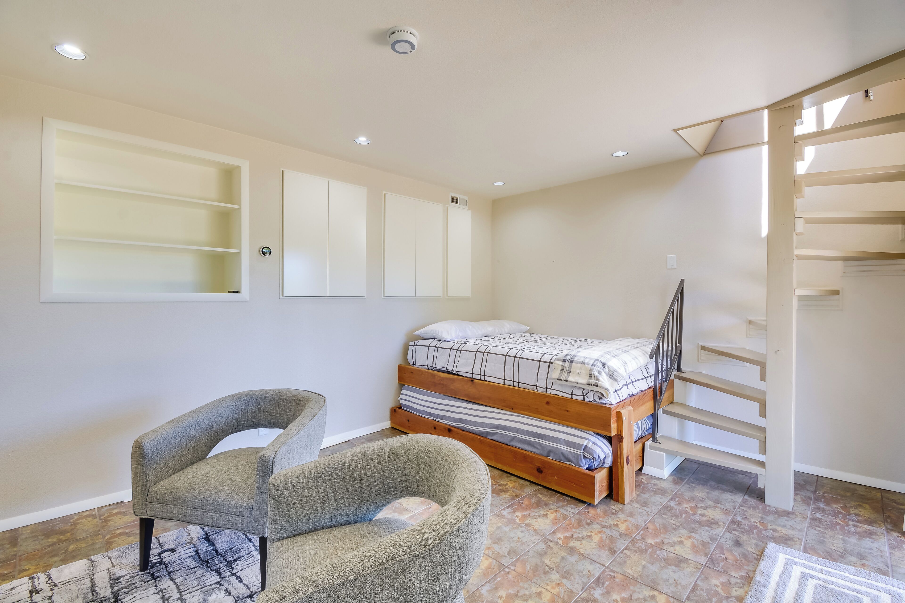 A bedroom with a bed, a chair, built-in shelves, a staircase, and a ceiling light.