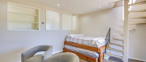 A bedroom with a bed, a chair, built-in shelves, a staircase, and a ceiling light.