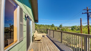 A wooden deck with a railing, a window with shutters, and a view of greenery in the background. - 1 Mi to Whiskey Row: Home w/ Fire Pit & Deck (Prescott)