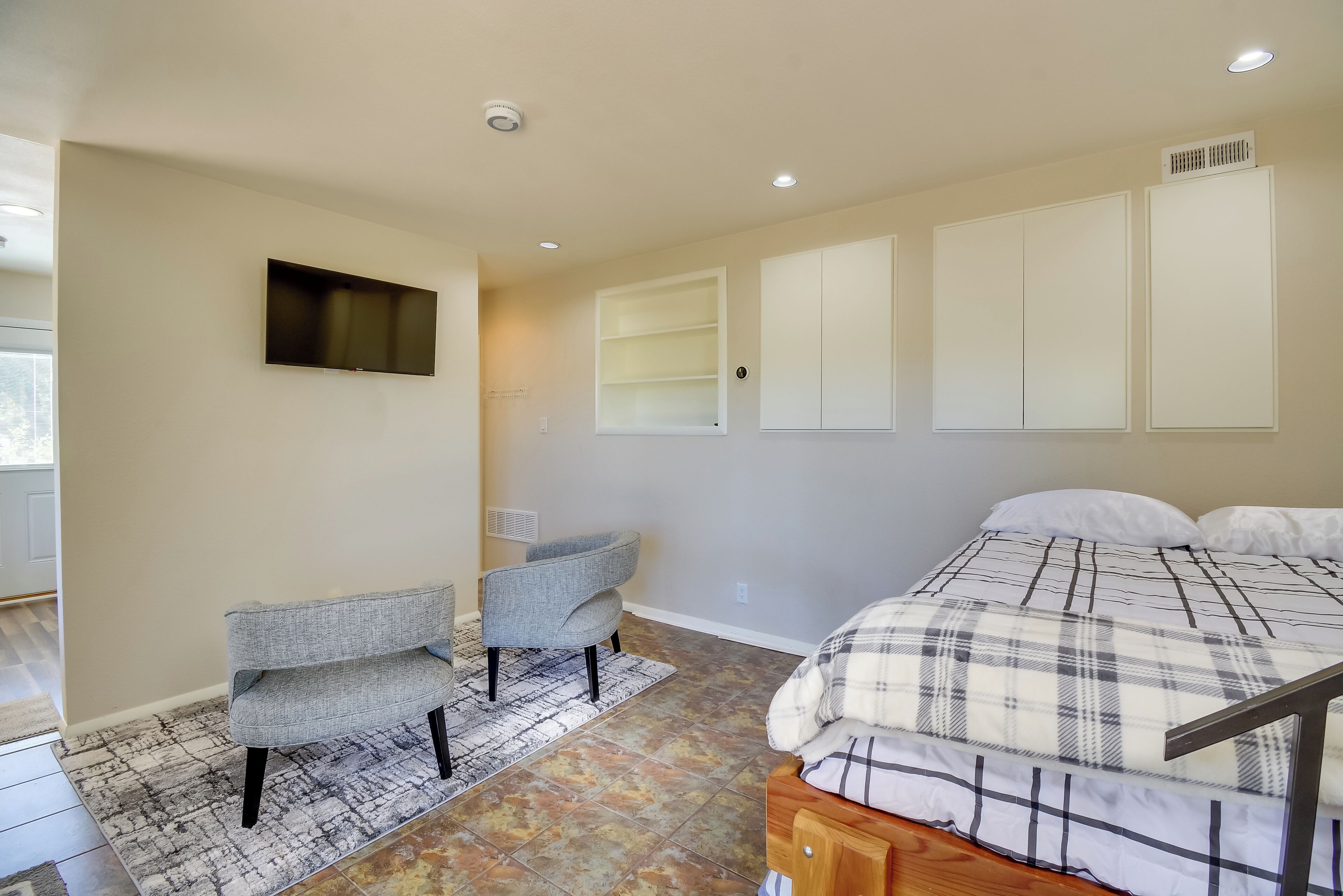 Un dormitorio con una cama, un sofá gris, un televisor montado en la pared y armarios empotrados.