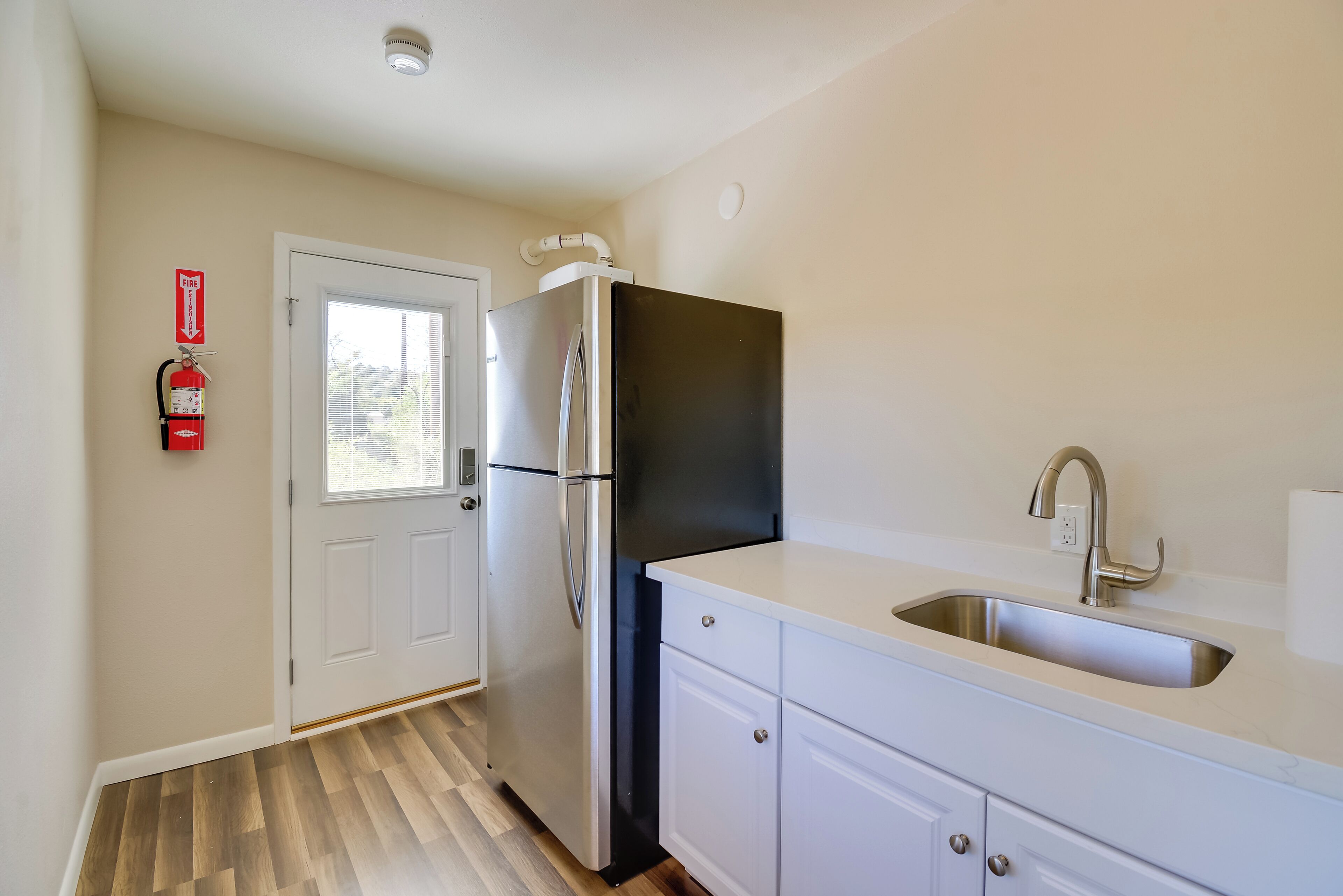 A kitchen with a stainless steel refrigerator, a white countertop, a sink, and a fire extinguisher on the wall.