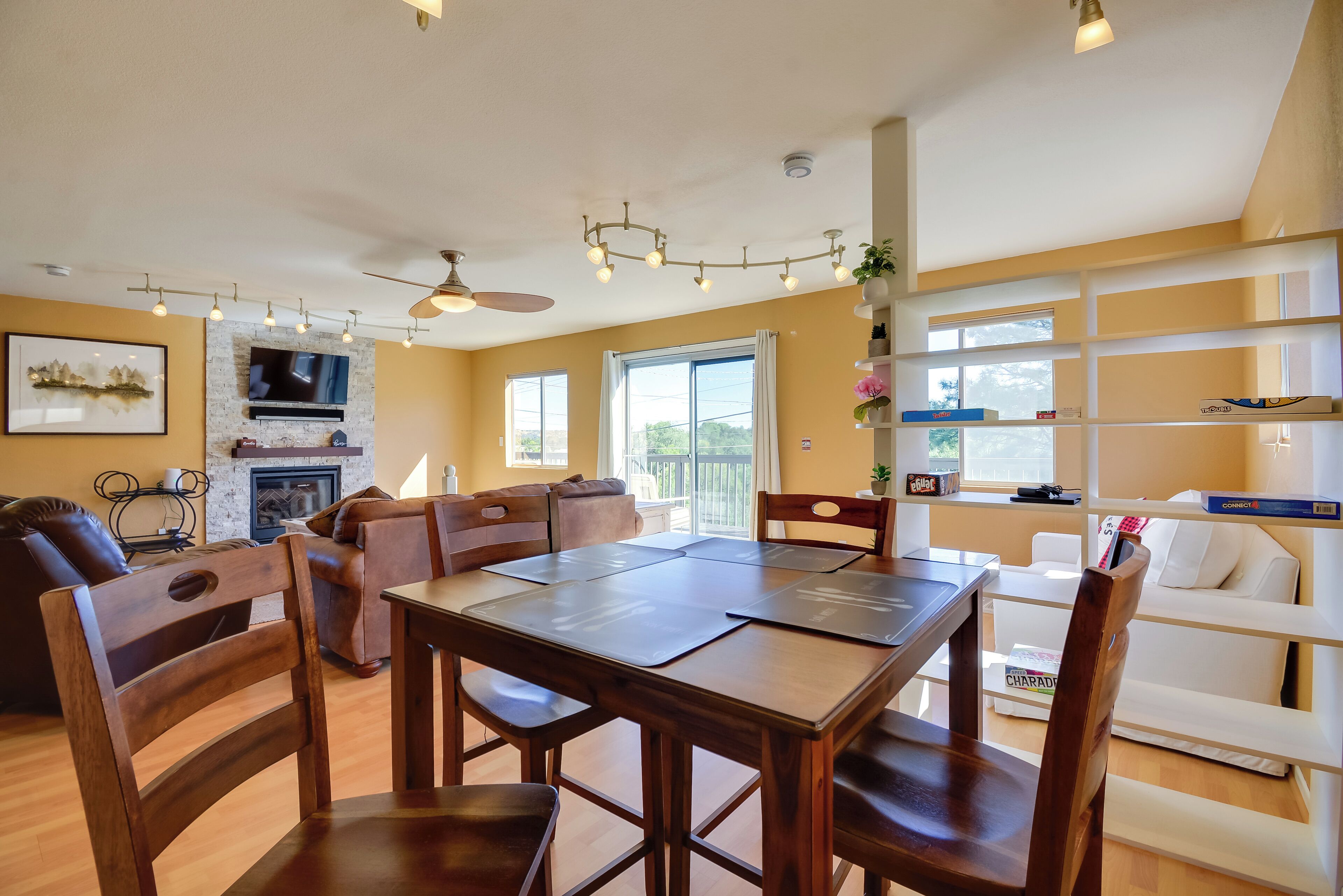 A spacious living area with a wooden dining table, comfortable seating, a fireplace, and a large window providing natural light.