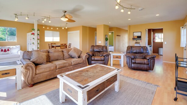 A living room with a brown leather sofa, a white coffee table, and a brown leather recliner. There is a white shelving unit with plants and a white couch with a red pillow. - 1 Mi to Whiskey Row: Home w/ Fire Pit & Deck (Prescott)