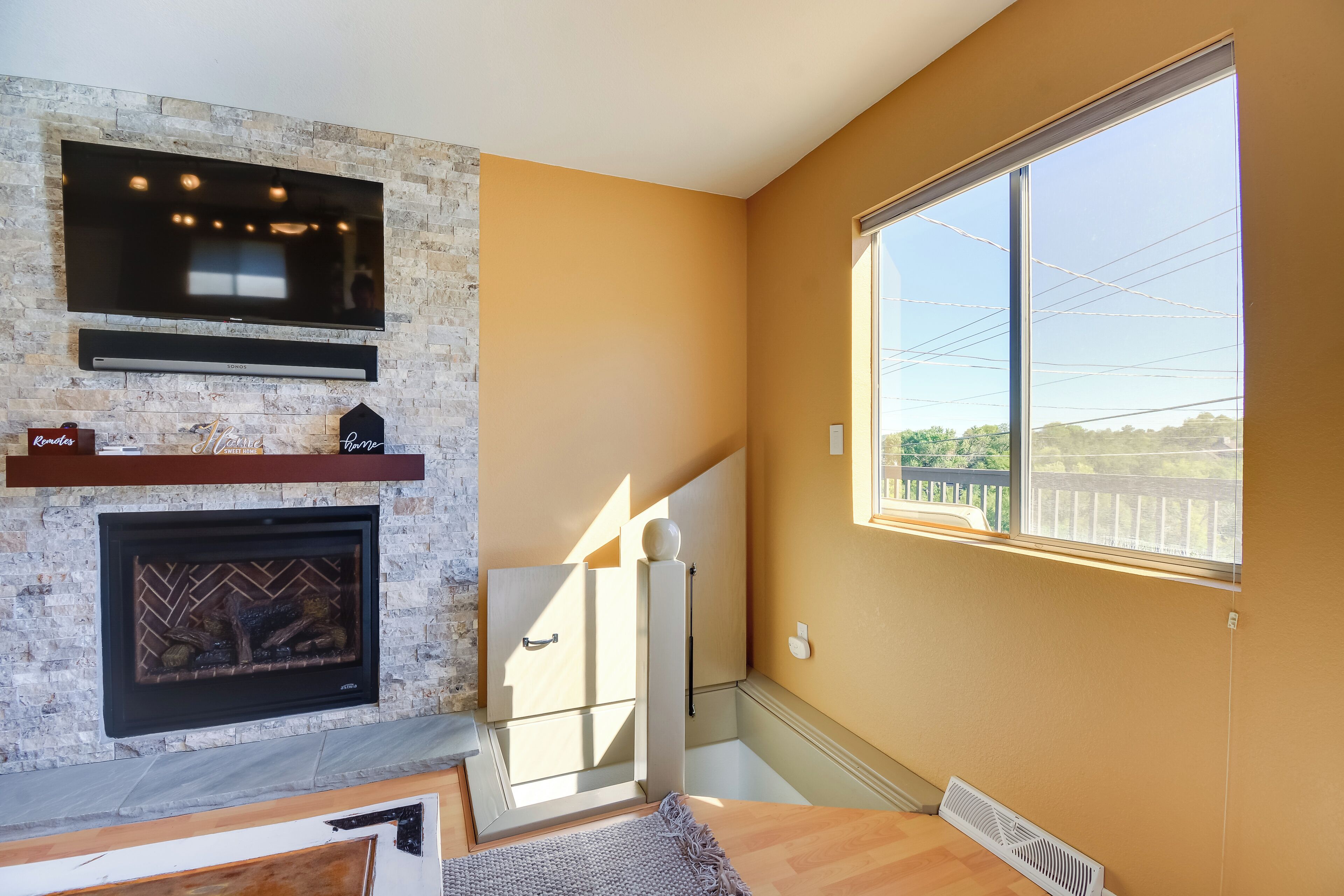 A living room with a stone fireplace, a mounted TV, and a large window with a view.