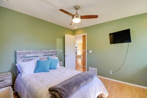 A bedroom with a wooden headboard, a bed with white and blue bedding, a ceiling fan, a TV mounted on the wall, and a wooden floor. - 1 Mi to Whiskey Row: Home w/ Fire Pit & Deck (Prescott)
