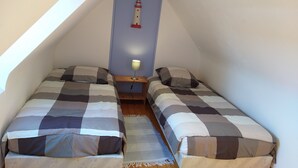 A small, cozy attic bedroom with two beds, a nightstand, a lamp, and a decorative lighthouse wall art.