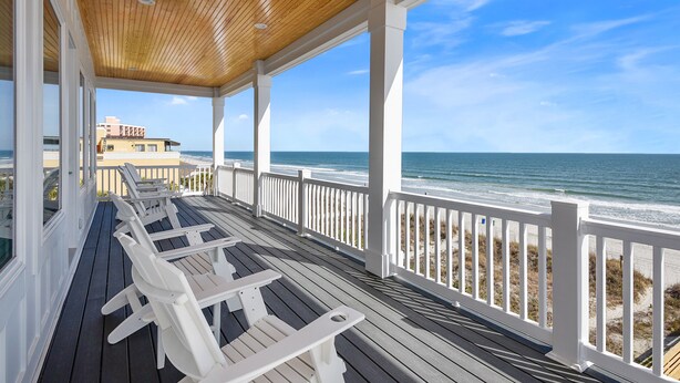 A covered deck with white chairs and a view of the ocean.