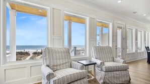 A room with large windows, two striped armchairs, a small table, and a view of the beach.