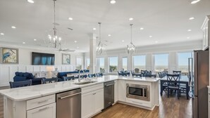 Una cocina amplia con una isla grande, muebles blancos, electrodomésticos de acero inoxidable y un comedor con sillas azules y una mesa.