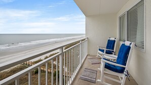 A balcony with a view of the beach, two blue chairs, and a window with blinds. - San A Bel 404 - Oceanfront Condo - Indoor Pool (North Myrtle Beach)