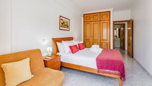 Habitación de hotel con cama, mesita de noche, armario de madera, puerta y baño visible a través de un acceso abierto.