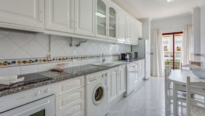 Una cocina moderna con armarios blancos, lavadora integrada y comedor con vistas.