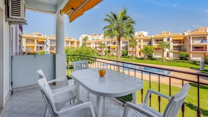 Un balcón con mesa y sillas, que da a una piscina y una zona residencial con varios edificios.