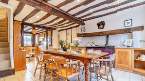 Un comedor amplio con una mesa y sillas de madera, una cocina al fondo y una escalera que sube a otro nivel.