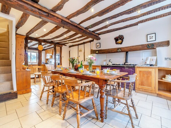 A spacious dining area with a wooden table and chairs, a kitchen in the background, and a staircase leading to another level.