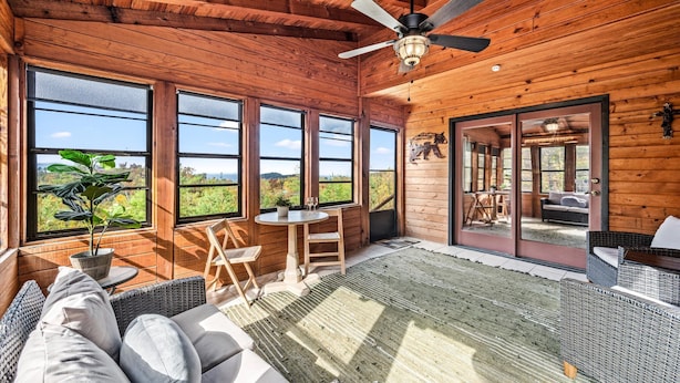 A wooden cabin interior with large windows, a ceiling fan, and a view of the outdoors. - Winter Wonderland of fun near Attractions (Sevierville)