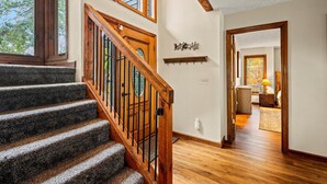 A staircase with wooden railings leading to a second floor, a wall-mounted coat rack, and a view into a room with a desk and lamp. - Winter Wonderland of fun near Attractions (Sevierville)