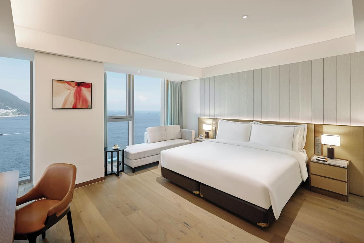 Ein modernes Hotelzimmer mit einem großen Bett, einer Couch, einem Schreibtisch und Meerblick.