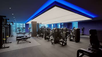 A modern gym with various exercise machines, a large mirror, and a view of the city through large windows.
